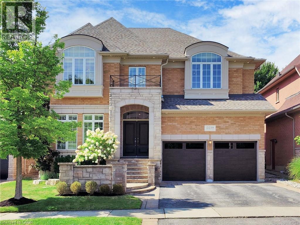 French country inspired facade featuring a shingled roof, stone siding, a garage, a balcony, and driveway