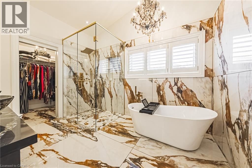 Full bathroom with marble tiled flooring, a spacious closet, a freestanding bath, a chandelier, and stone wall