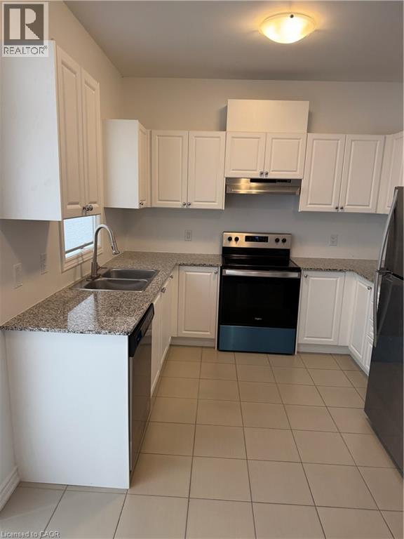 Kitchen featuring stainless steel appliances, white cabinets, dark stone counters, and light tile patterned floors
