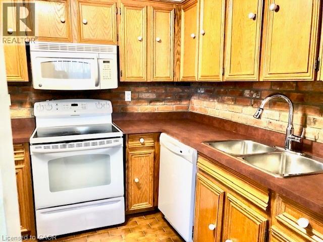 Kitchen featuring white appliances, dark countertops, and wood finish cabinets