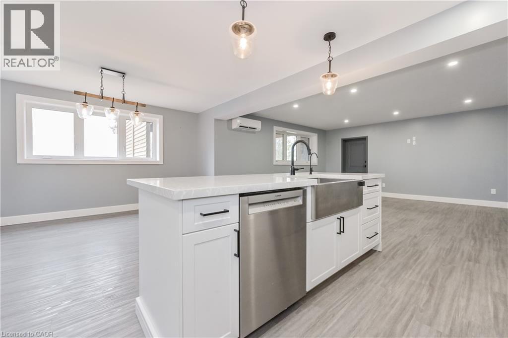 Kitchen featuring dishwasher, a wall mounted air conditioner, light countertops, decorative light fixtures, and a center island with sink