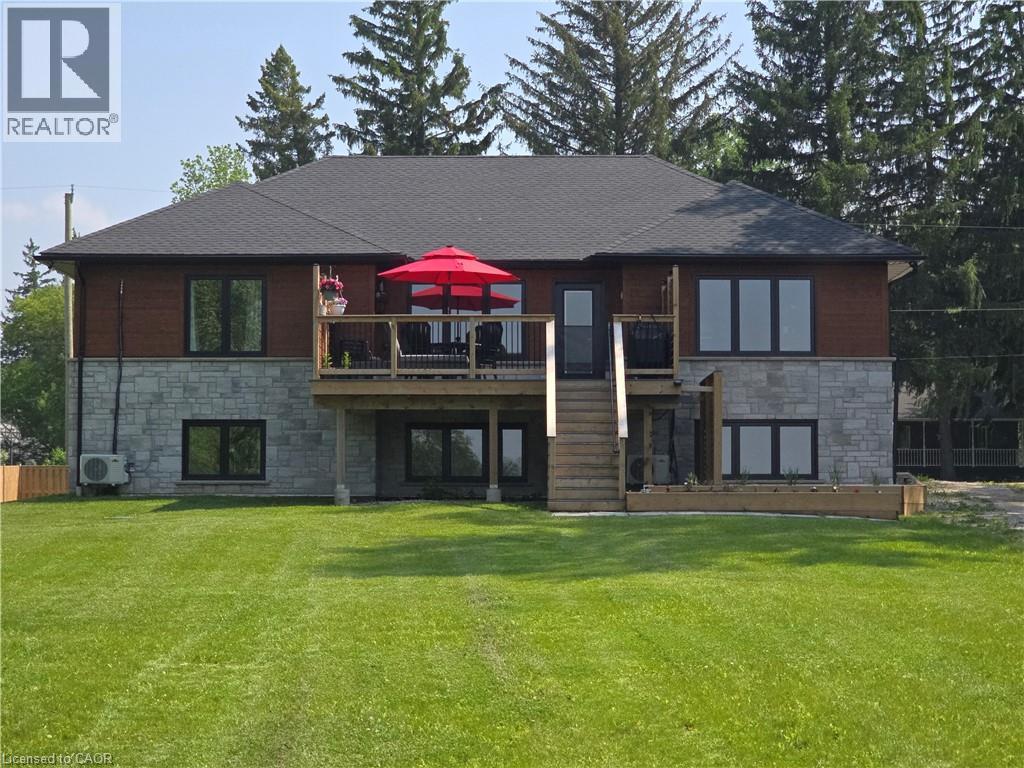 Rear view of house featuring stone siding, a deck, a lawn, and a shingled roof