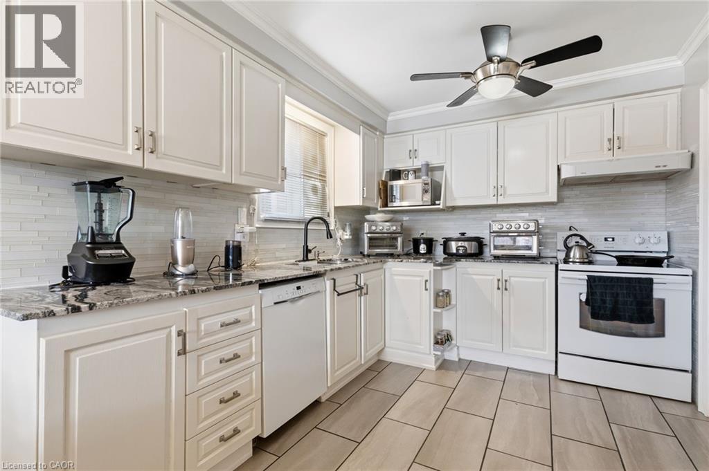 Kitchen featuring white appliances, white cabinets, light stone countertops, ceiling fan, and crown molding