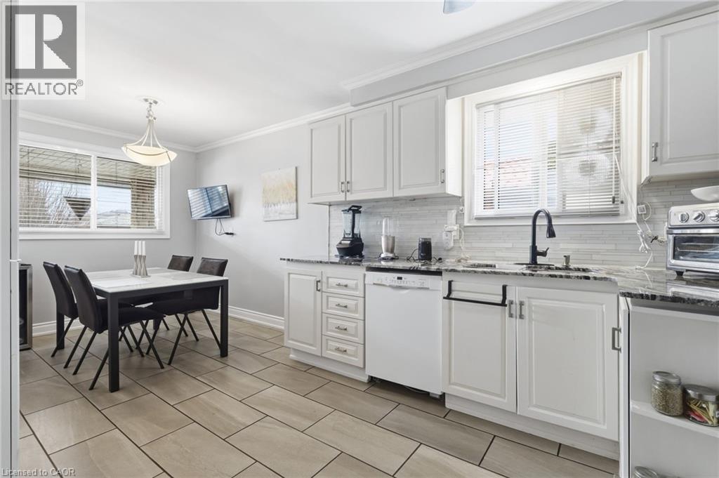 Kitchen with crown molding, light stone countertops, white dishwasher, white cabinetry, and decorative light fixtures