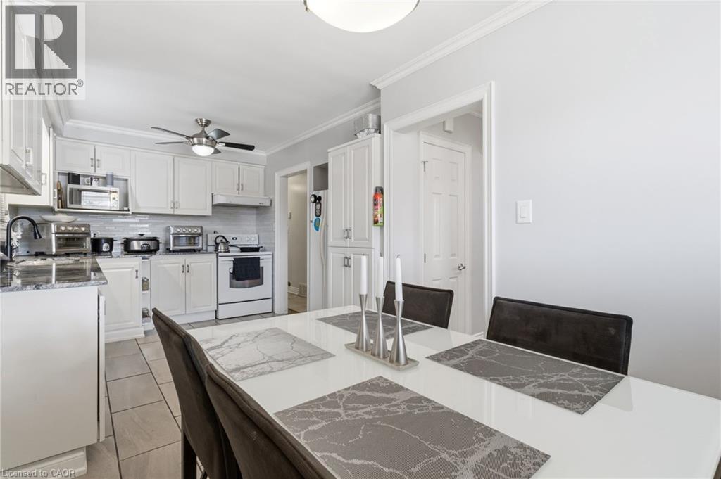 Kitchen with ornamental molding, white cabinets, white appliances, light stone countertops, and ceiling fan