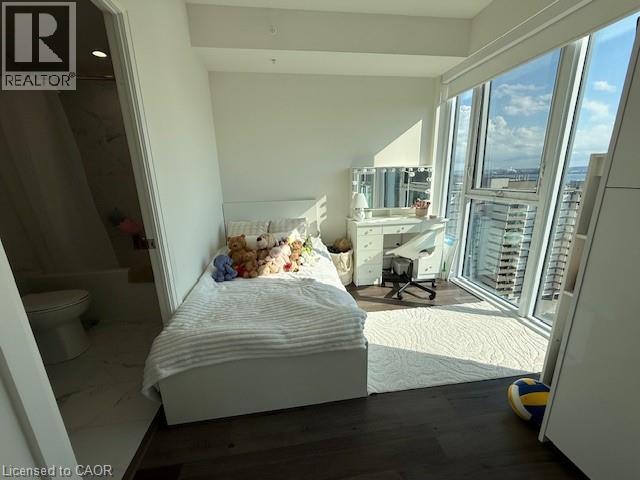 This bright room features expansive windows offering city and water views, dark wood flooring, and a white area rug
