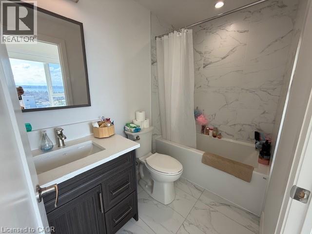 The bathroom features a modern vanity with a white countertop and dark wood cabinetry, a white toilet, and a bathtub with a shower featuring white and grey marbled tile surround