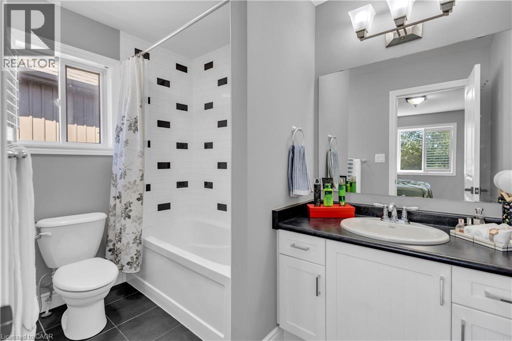 Ensuite bathroom featuring vanity, shower / bathtub combination with curtain, and dark tile patterned flooring