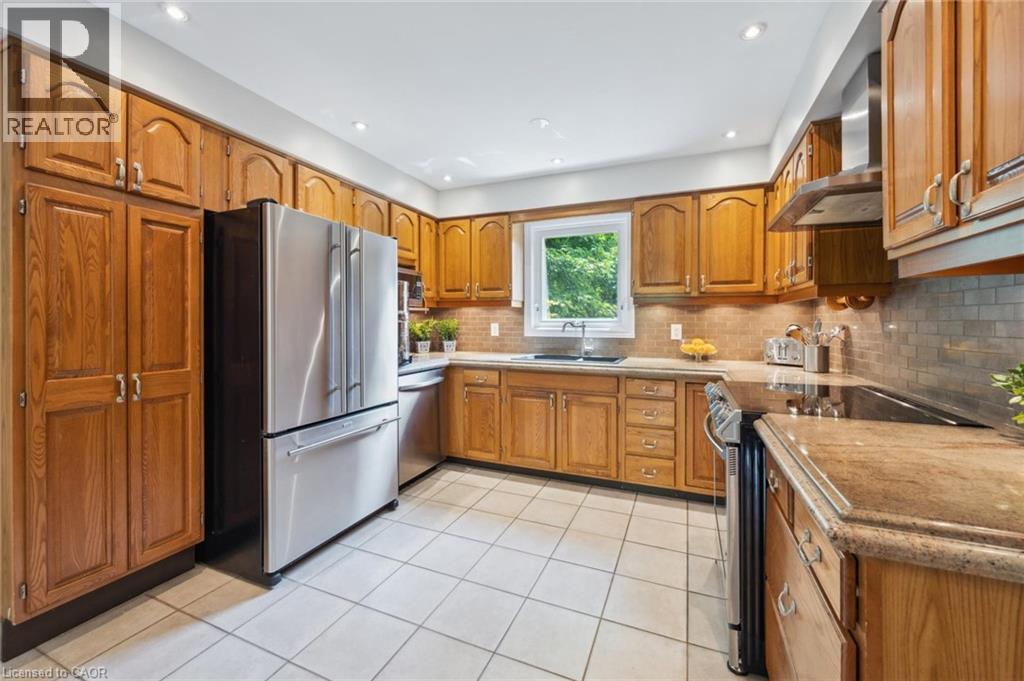 Kitchen with stainless steel appliances, wood finish cabinetry, light tile patterned floors, recessed lighting, and light stone counters