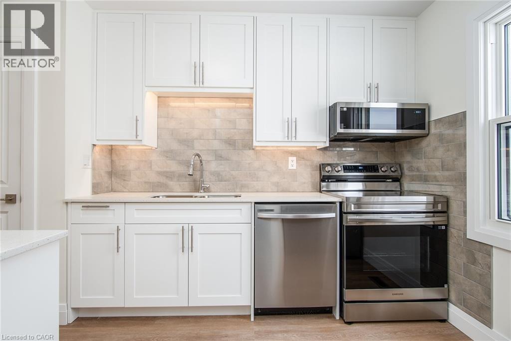 Kitchen with stainless steel appliances, white cabinets, light stone countertops, and light wood-style floors