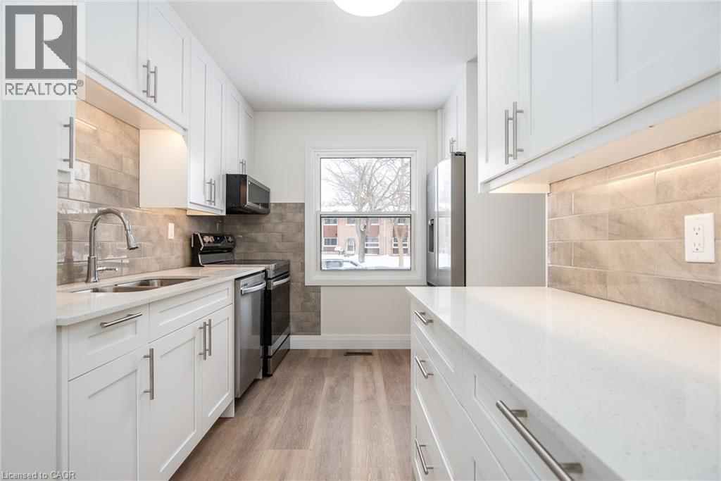 Kitchen featuring white cabinetry, light stone counters, stainless steel appliances, light wood finished floors, and tasteful backsplash