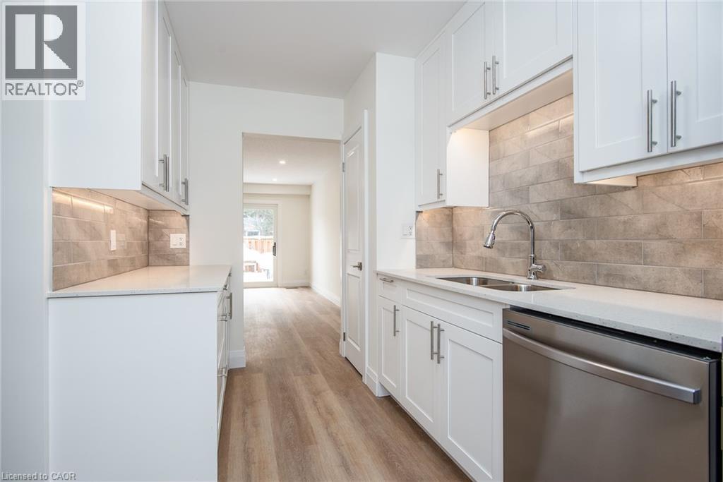 Kitchen featuring stainless steel dishwasher, white cabinets, light stone countertops, light wood finished floors, and tasteful backsplash