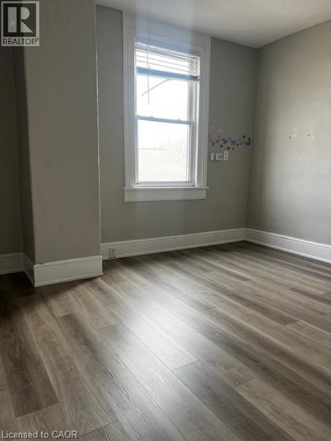 This room features light grey walls, a single window with blinds, and durable wood-look flooring