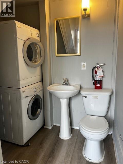 Utility space featuring a stacked washer and dryer, a pedestal sink, and a toilet