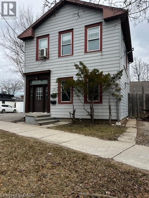 The property features a two-story facade with light gray siding and dark red trim around the windows and eaves