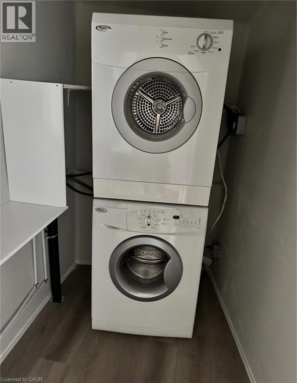 Laundry area featuring a stacked washer and dryer, wood-look flooring, and a white shelf