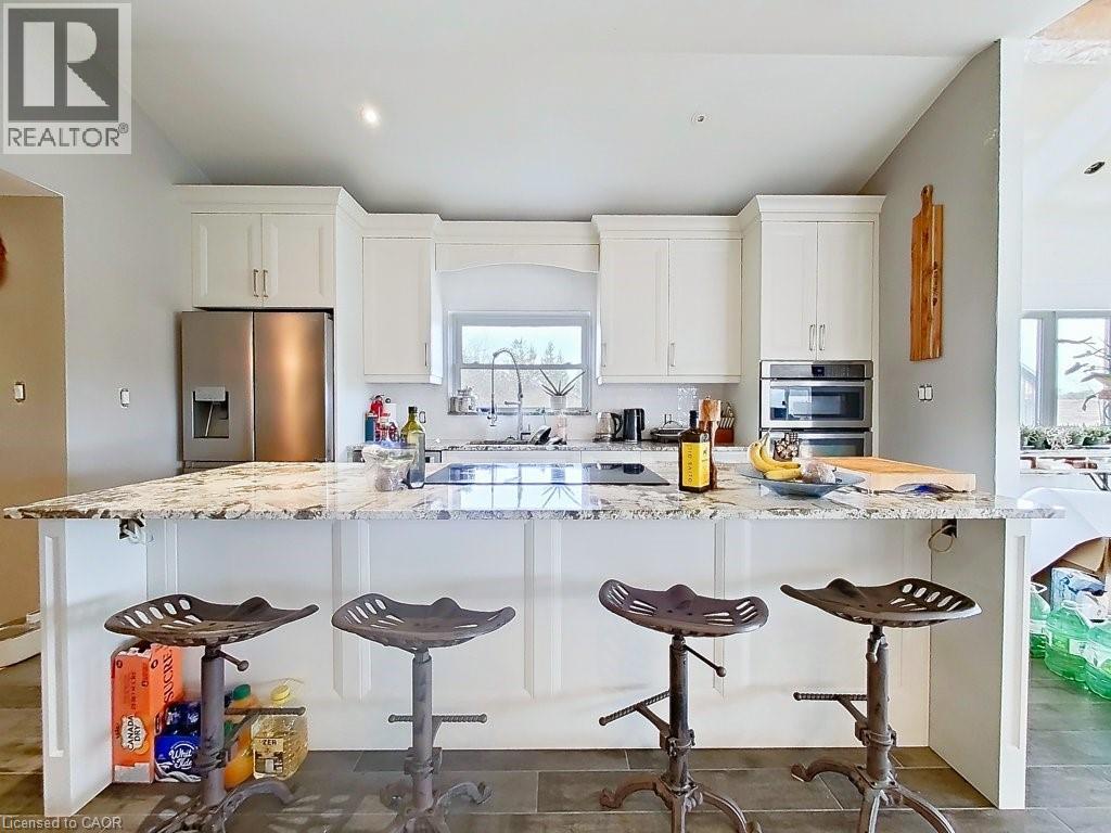 The kitchen features white cabinetry, stainless steel appliances including a refrigerator and built-in oven, and a spacious island with a light-colored granite countertop