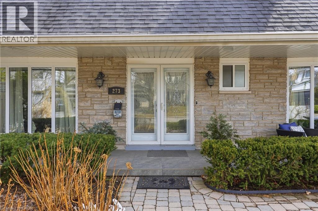 View of exterior entry featuring a porch, a shingled roof, and stone siding