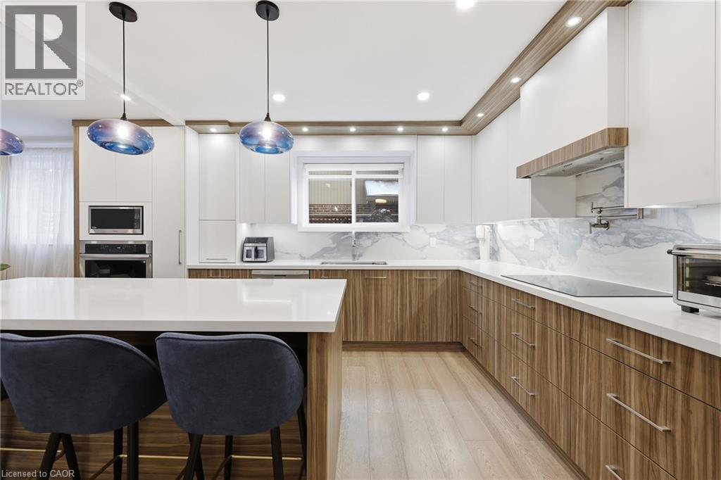 Two tone kitchen with two tone cabinetry, a kitchen breakfast bar, modern cabinets, stainless steel appliances, and light wood finished floors
