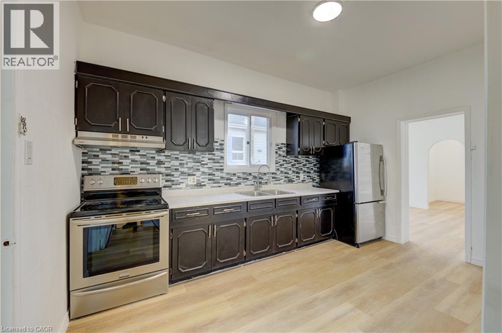 The kitchen features dark cabinetry, a mosaic tile backsplash, and stainless steel appliances including a range and refrigerator