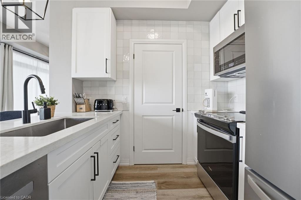 Kitchen featuring stainless steel appliances, white cabinets, light stone countertops, and light wood-type flooring