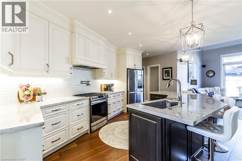 Two tone kitchen featuring a center island with sink, light stone counters, stainless steel appliances, a kitchen breakfast bar, and dark wood finished floors
