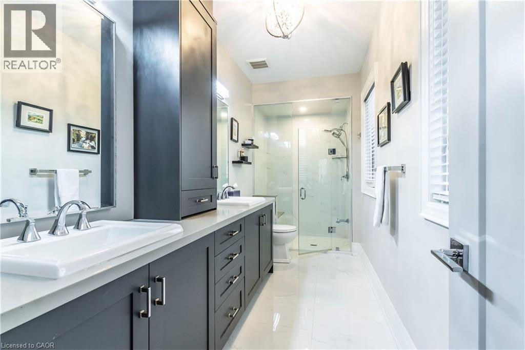 Full bath featuring double vanity, a marble finish shower, light marble finish flooring, and a chandelier