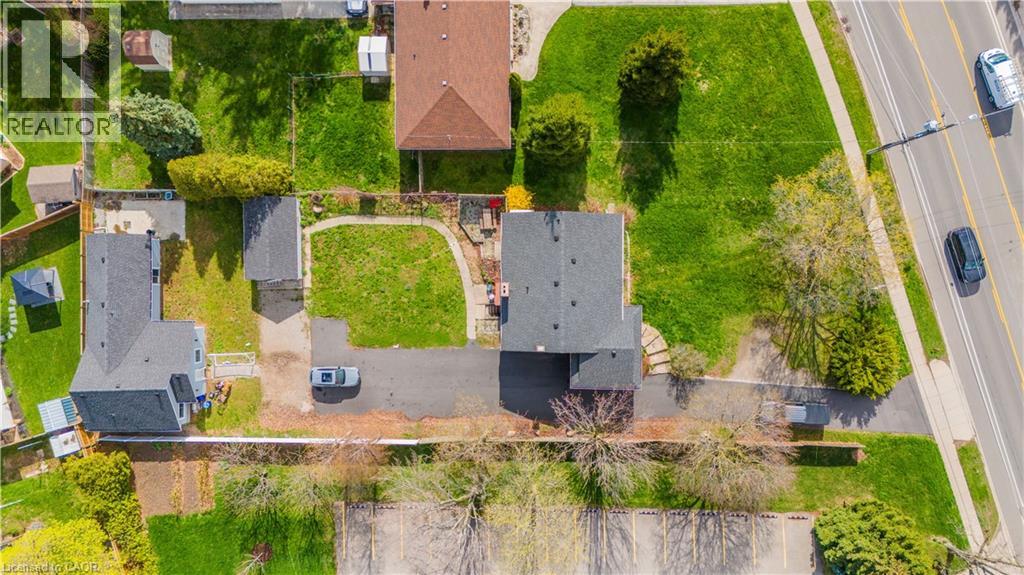 Aerial view showcasing two residential structures with dark shingle roofs, surrounded by expansive green lawns