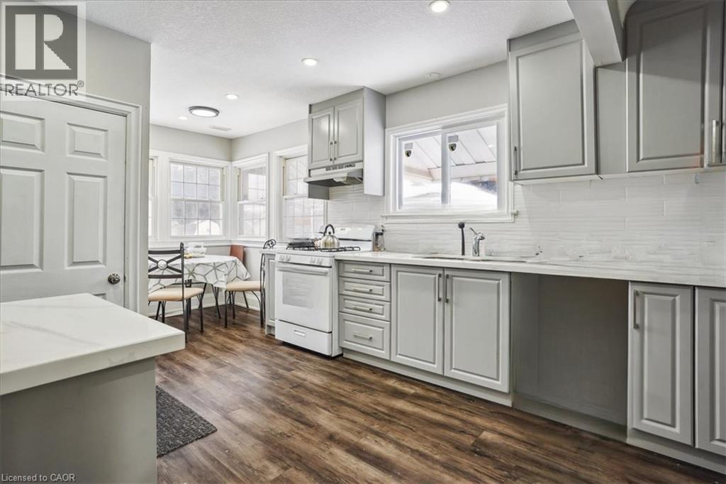 Kitchen featuring gray cabinets, white range with gas stovetop, dark wood-style floors, decorative backsplash, and recessed lighting