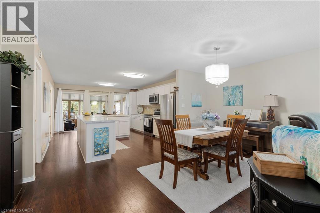 This open concept living space features dark hardwood floors, a kitchen with white cabinetry and stainless steel appliances, and a dining area with a chandelier
