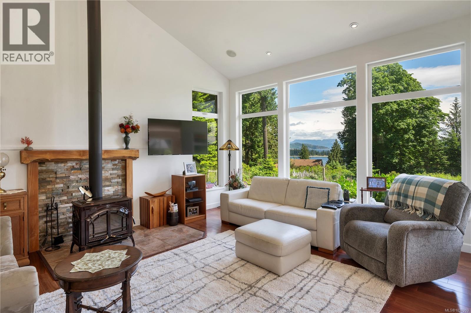 living room on the main floor, woodstove on brick hearth, floor to ceiling windows & ocean views over Drew Harbour & Rebecca Spit!