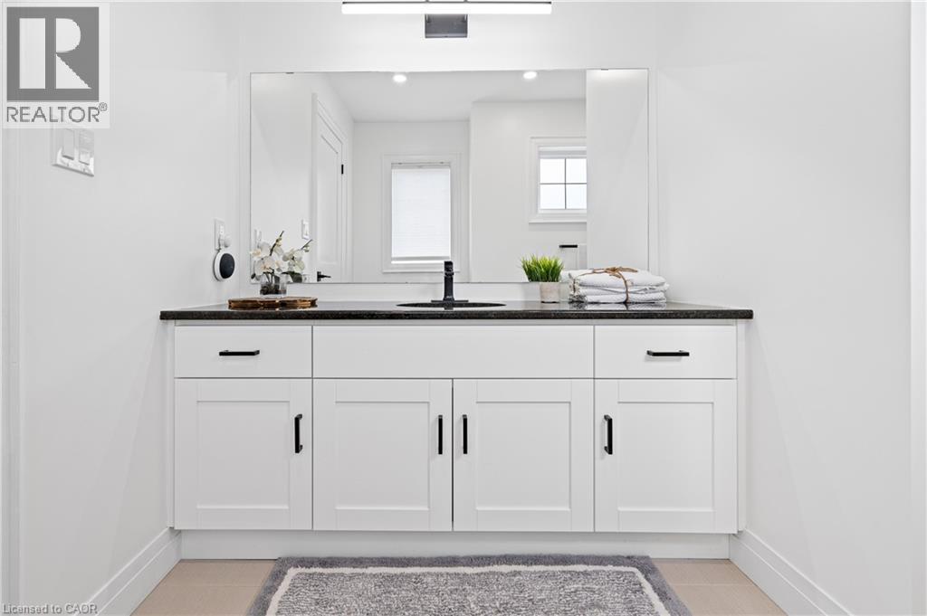 Modern bathroom vanity featuring white shaker cabinetry with black hardware, a dark countertop, an undermount sink with a matte black faucet, and a large mirror