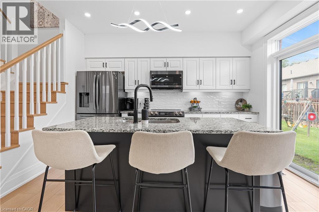 Modern kitchen featuring a black island with a speckled countertop, white cabinetry with black hardware, and stainless steel appliances