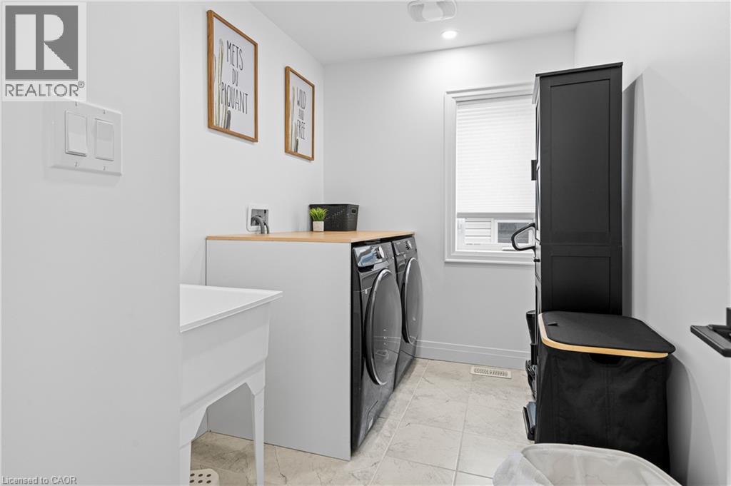 Functional laundry area featuring light-toned tile flooring, a utility sink, and a countertop with wood-finish surface