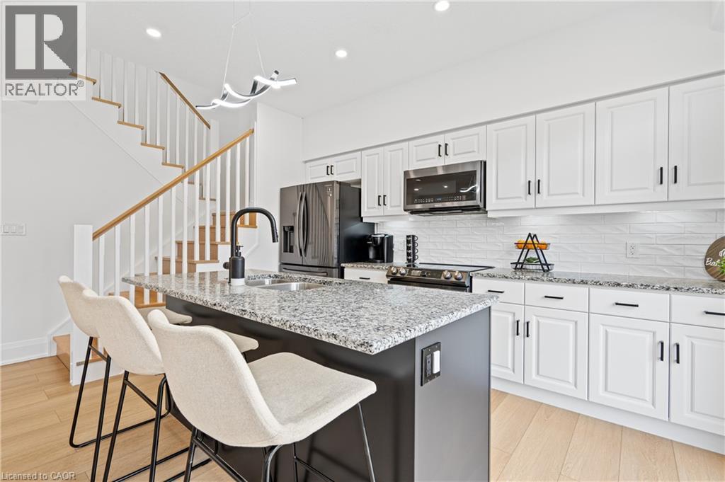 Modern kitchen featuring a central island with a sink, white cabinetry, integrated stainless steel appliances, and wood-finish flooring