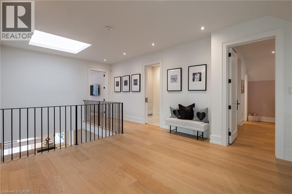 Upper-level hallway featuring a skylight, recessed lighting, light wood-finish flooring, and a black wrought iron railing