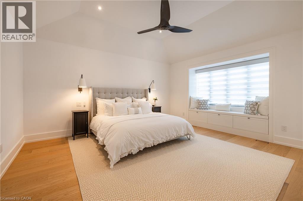 Vaulted ceiling bedroom featuring wood-finish flooring, a broad window with a built-in bench and storage, and wall-mounted sconce lighting