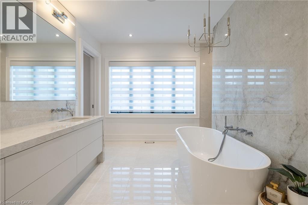 Freestanding soaking tub with a wall-mounted faucet, complemented by a large format tiled accent wall and polished floor tiles