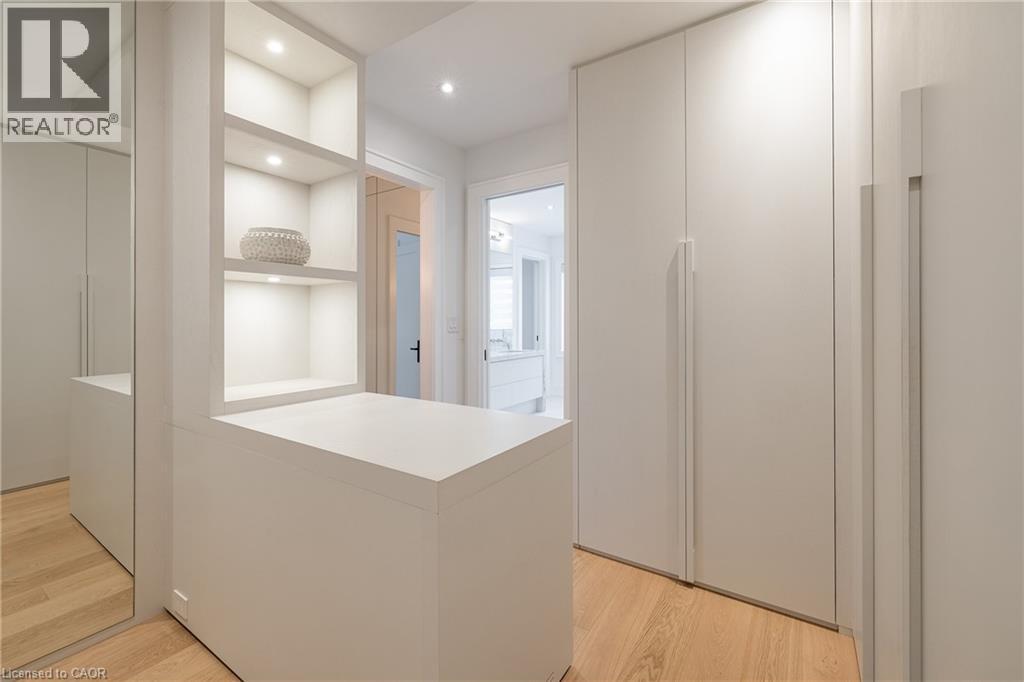 Walk-in closet featuring light wood-finish flooring, built-in cabinetry with integrated shelving, recessed lighting, and a full-length mirrored panel