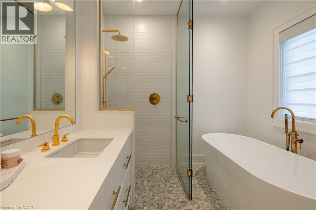 Bathroom featuring a freestanding soaking tub with floor-mounted brass fixture, a glass-enclosed shower with subway tile surround and brass fixtures, and a vanity with an integrated sink and brass fau