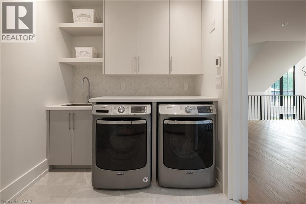 Dedicated laundry area featuring a utility sink with a gooseneck faucet, light-toned shaker-style cabinetry, open shelving, and a patterned tile backsplash