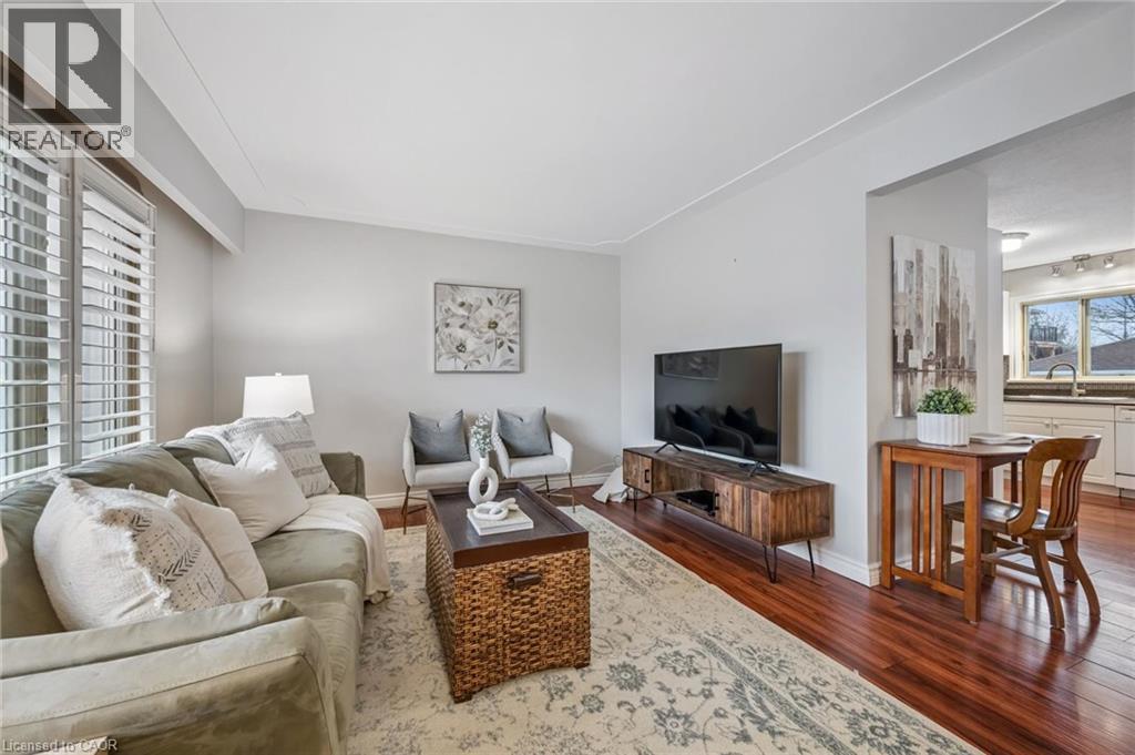 Living area with wood-finish flooring, white plantation shutters, and crown molding