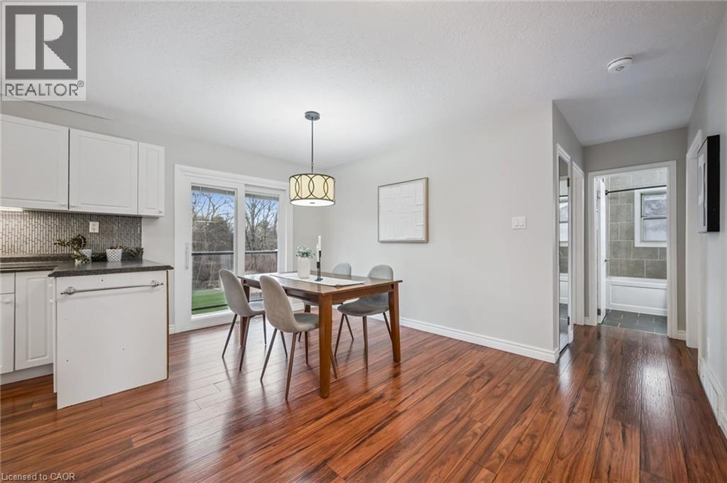 Bright dining area featuring wood-finish flooring, a contemporary pendant light fixture, and sliding glass doors that open to exterior green space