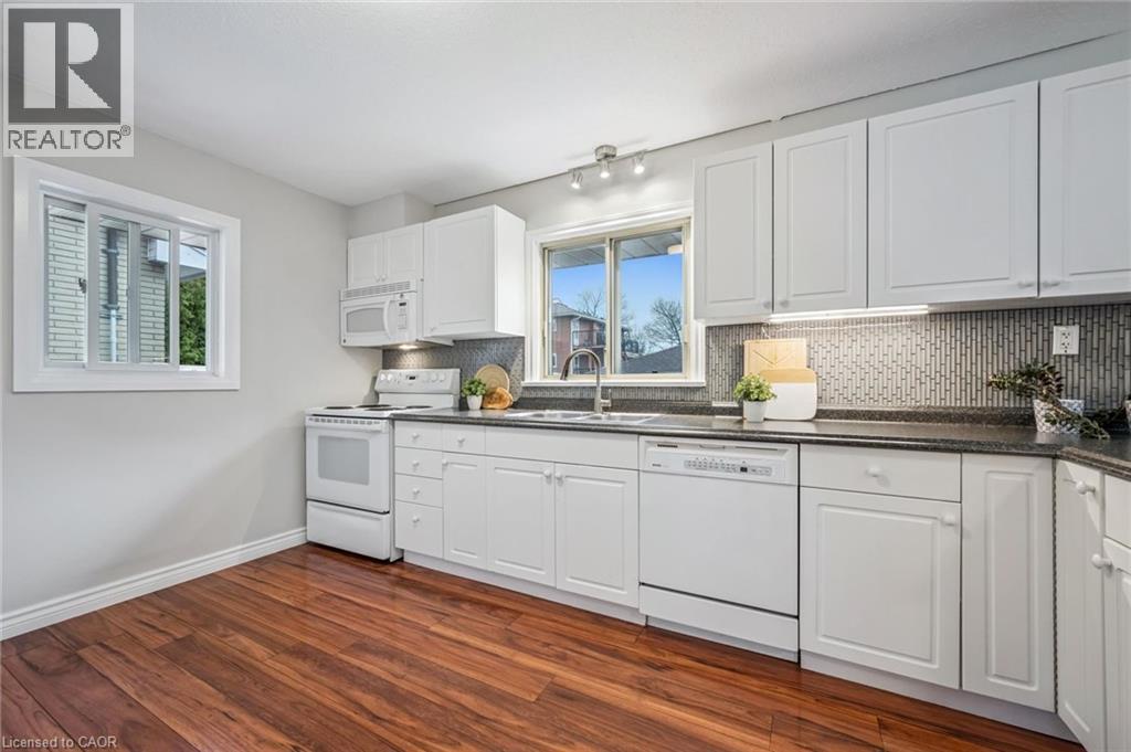 Bright kitchen featuring white cabinetry, dark countertops, a mosaic tile backsplash, stainless steel sink, and wood-finish flooring