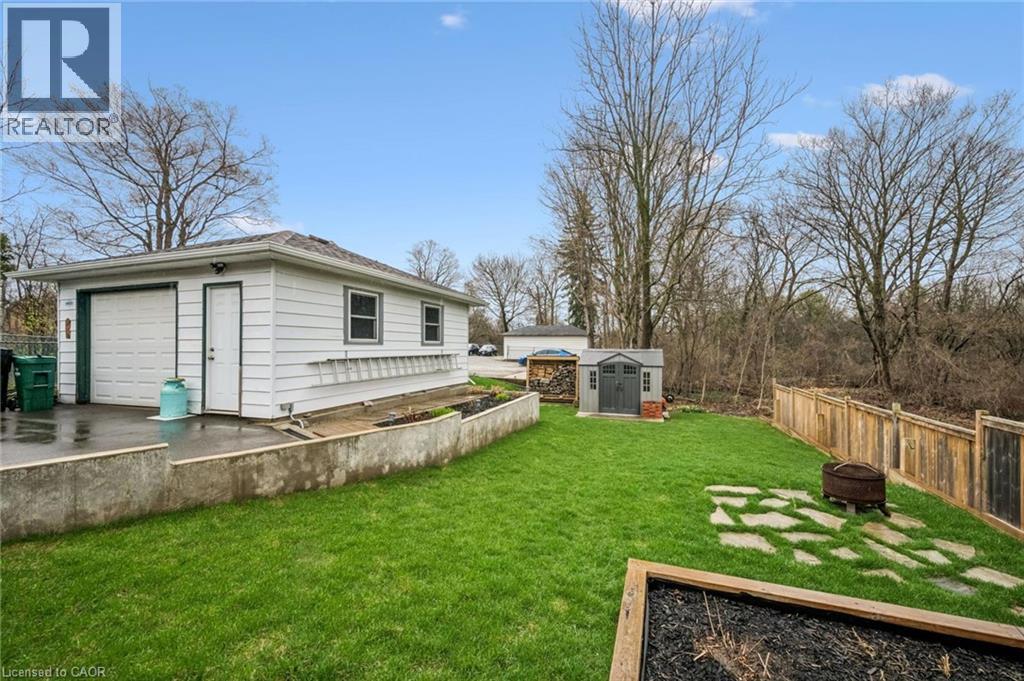 Detached garage with a white overhead door and side entry, complemented by a manicured lawn, a wooden privacy fence, and a garden shed