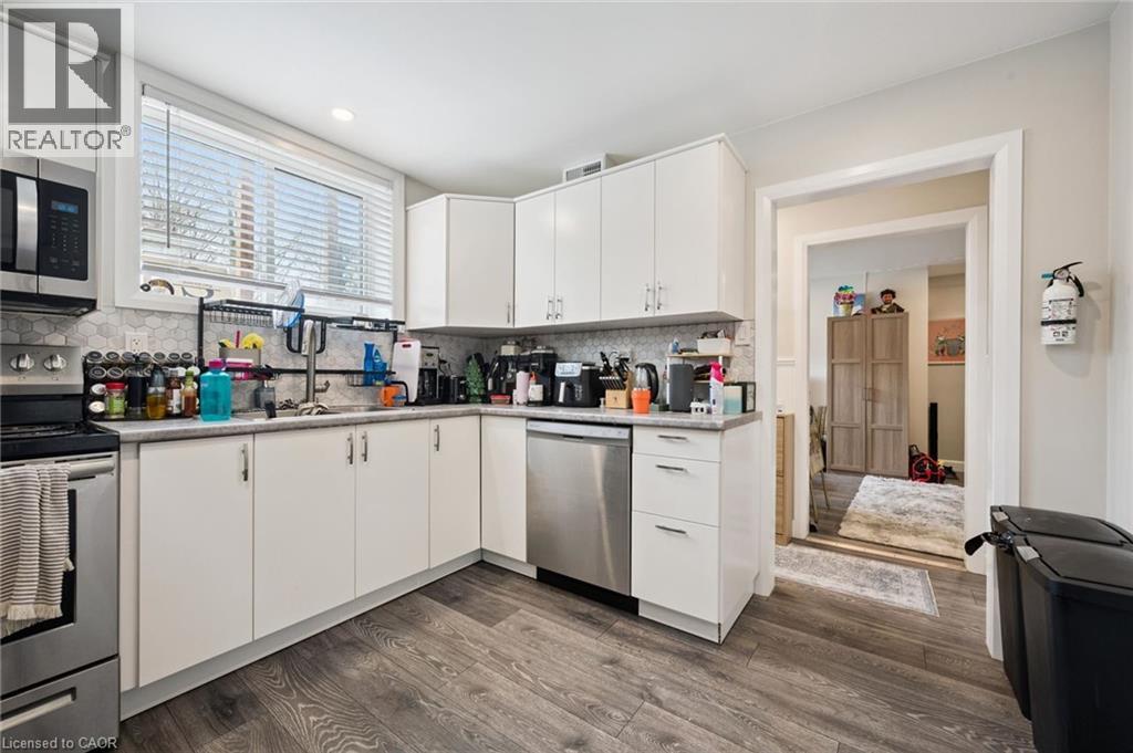 Corner kitchen featuring white cabinetry, stainless steel appliances, wood-finish flooring, a mosaic tile backsplash, and a window with blinds