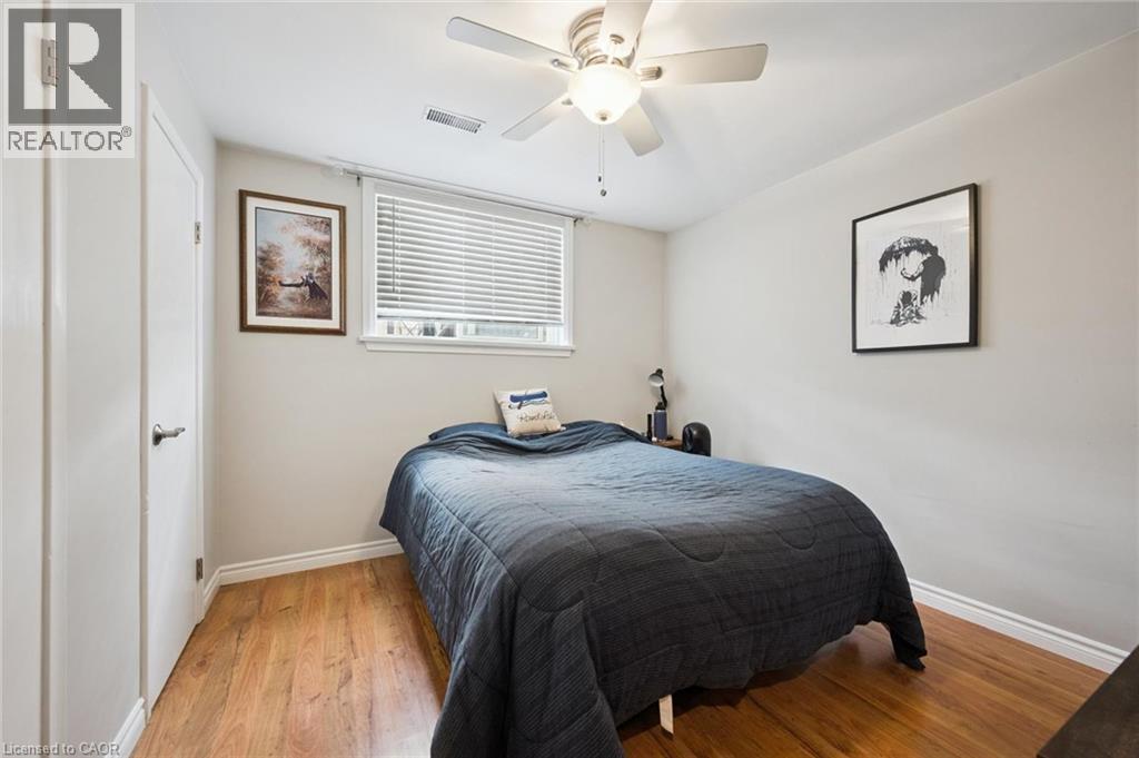 Bedroom featuring wood-finish flooring, a ceiling fan with integrated lighting, a window with horizontal blinds, and a white interior door with contemporary hardware