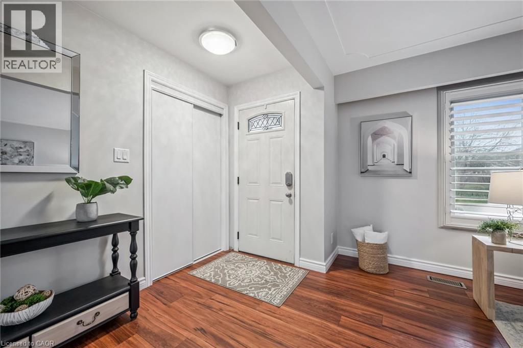 Entryway featuring rich wood-finish flooring, a white paneled entry door with decorative glass, and a window with horizontal blinds