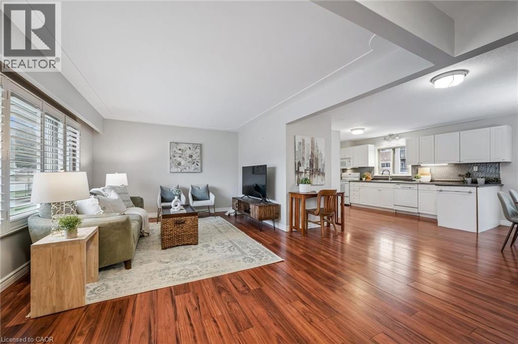 Open-concept living space featuring rich wood-finish flooring, white plantation shutters, and a kitchen with white cabinetry, black countertops, and a patterned backsplash