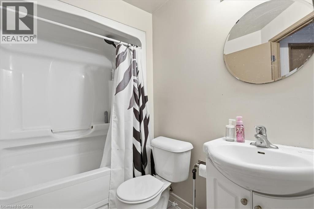 Bathroom featuring a white bathtub with a shower, a toilet, a vanity with an integrated sink, and an oval mirror